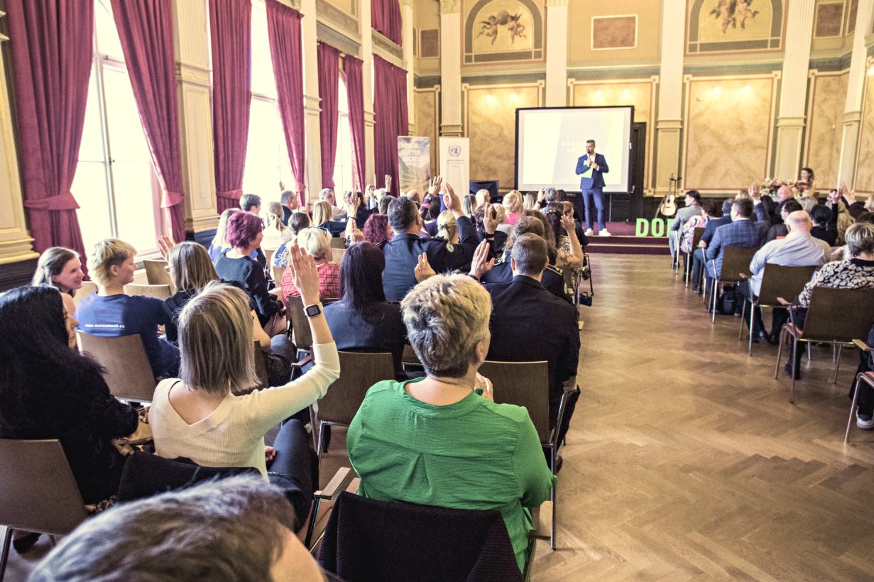 Moderátor konference Ondra Vodný na pódiu, sál s publikem